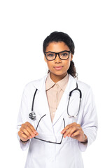 Fototapeta premium African american ophthalmologist in white coat holding eyeglasses and looking at camera isolated on white.