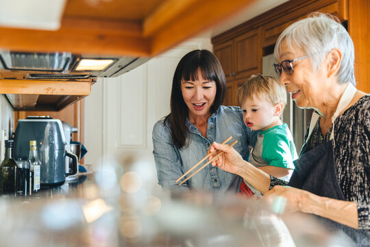 Woman And Son Looking At Mother Cooking With Chopsticks