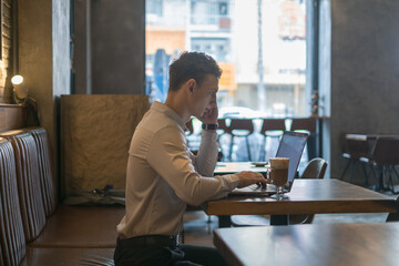 Freelancer working in coffee shop with a laptop. Thinking, solving problems, new ideas. Young business man surfing the net on laptop in a bar. 