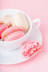 Pink and cream color macarons in a white porcelain cup on a pink background
