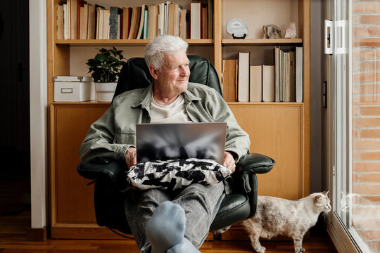 Smiling senior man with cat looking through window at home