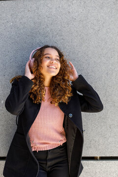 Young woman listening music through headphones in front of wall