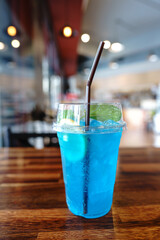 A plastic glass of blue lemon soda with a brown straw put on wooden table in the cafe.