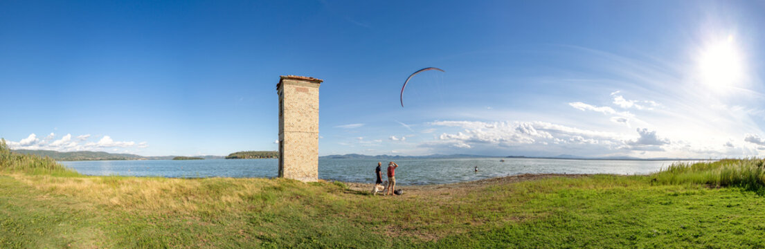 Senior man with son watching kiteboarding by Lake Trasimeno during sunny day
