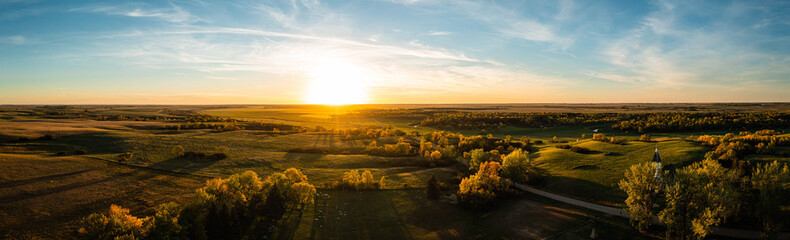Aerial panorama of a sunset over the gentle rolling hills of the Great Plains with trees in their...