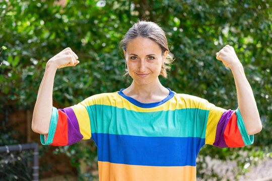 Beautiful mid adult woman wearing multi colored top flexing biceps in garden