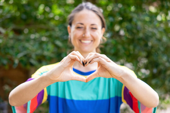 Smiling woman gesturing heart shape in garden - Powered by Adobe