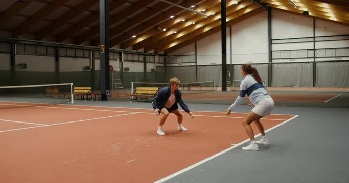 A man and woman throwing tennis balls to each other, hitting them on the floor