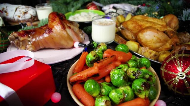 Woman set festive Christmas dinner table with traditional foods and dished &ndash; baked ham, chicken, roasted carrots and brussels sprouts, potato, with Xmas decor and gifts. Preparation fod Christmas dinn