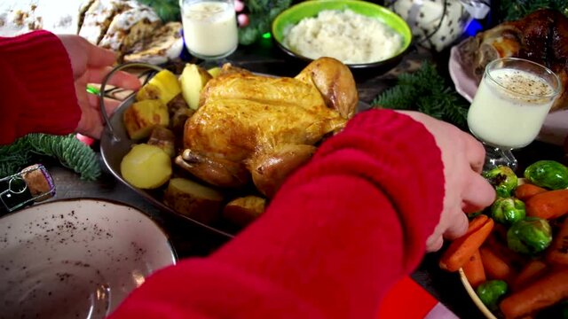 Woman set festive Christmas dinner table with traditional foods and dished – baked ham, chicken, roasted carrots and brussels sprouts, potato, with Xmas decor and gifts. Preparation fod Christmas dinn