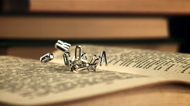 English letters fall on an open book. On a black background. Filmed is slow motion 1000 frames per second. High quality FullHD footage