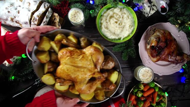 Woman set festive Christmas dinner table with traditional foods and dished &ndash; baked ham, chicken, roasted carrots and brussels sprouts, potato, with Xmas decor and gifts. Preparation fod Christmas dinn