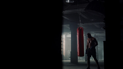 Man finishing boxing training. Boxer walking in loft building with punching bag