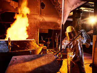 Worker holding metal rod in furnace at foundry
