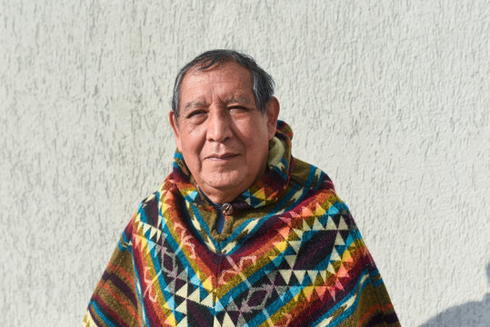 Senior indigenous man wearing poncho in front of wall