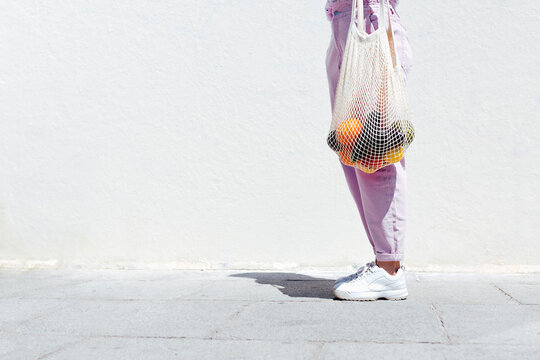 Woman holding bag of fruits by white wall