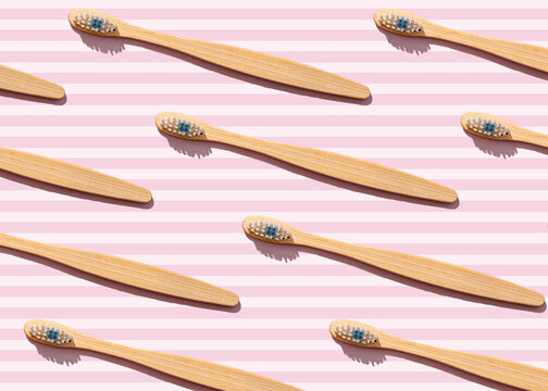 Pattern of wooden toothbrushes flat laid against pink striped background