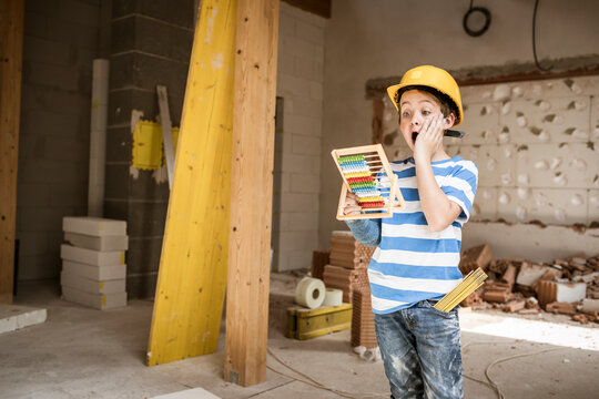 Surprised boy holding abacus toy during rebuilding house
