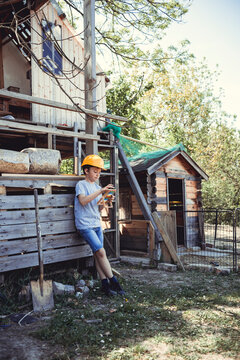 Boy in yellow hardhat calculating on toy while leaning on rabbit hutch in back yard