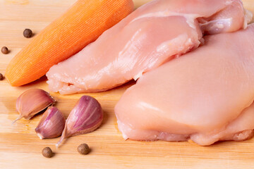 Raw chicken fillet on a cutting board. Chilled chicken breast, carrot and pepper top view