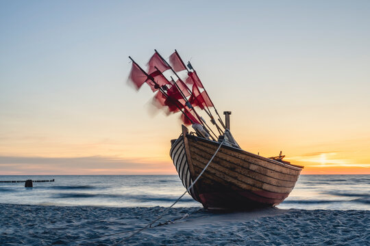 Lone fishing boat left on sandy shore at sunset