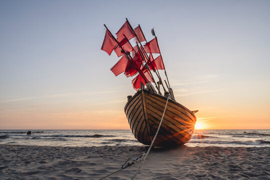 Lone fishing boat left on sandy shore at sunset
