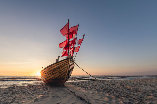 Lone fishing boat left on sandy shore at sunset