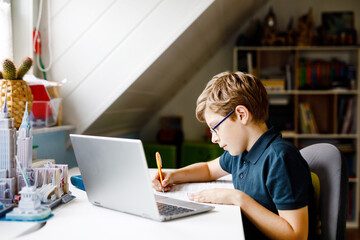 Kid boy with glasses learning at home on laptop for school. Adorable child making homework and...