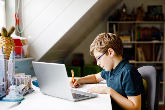 Kid boy with glasses learning at home on laptop for school. Adorable child making homework and using notebook and modern gadgets. Home schooling concept.