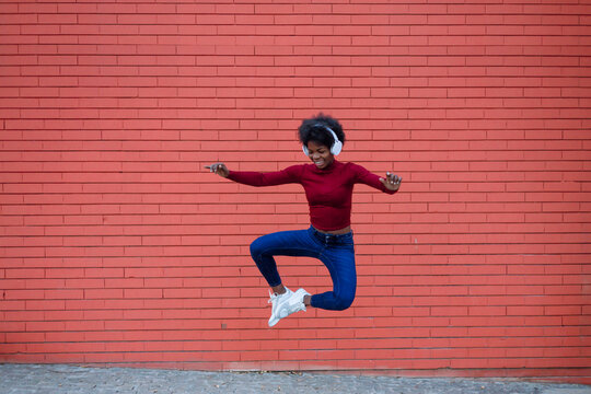 Young woman heel clicking in front of brick wall