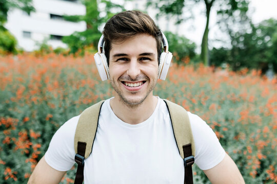 Smiling young man listening music through headphones amidst meadow