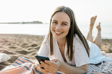 Smiling woman holding mobile phone while relaxing at beach