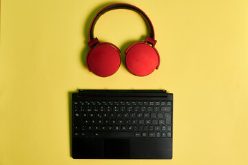 Computer keyboard and red headphones on a yellow background