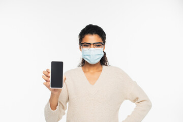 African american woman in eyeglasses and medical mask holding cellphone with blank screen isolated on white.