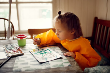 cute caucasian child Toddler is engaged in creativity in a yellow protective apron, the child draws with paints on salt, unusual drawing and developmental activities