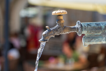 Vintage animal head brass tap with drinking water on the city street, Italy