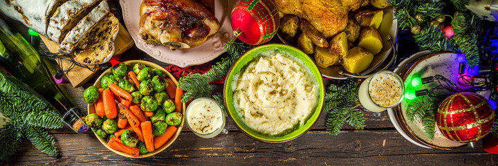 Festive Christmas dinner table with traditional foods and dished – baked ham, chicken, roasted carrots and brussels sprouts, potato, with Christmas decor and gifts 
