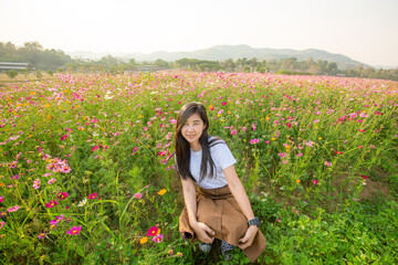 Asian girl in white dress sits in a meadow of pink flowers in the countryside in summer with copy space for graphic design.