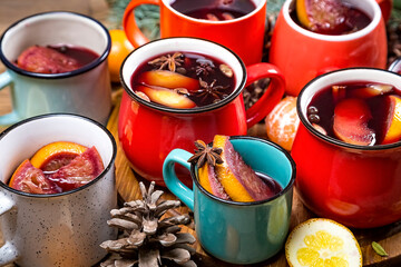 Close up top view of colorful cups of traditional Christmas drink mulled red spiced wine with cinnamon stick, apples and citrus on wooden table with star anise and christmas fir tree. Christmas party.