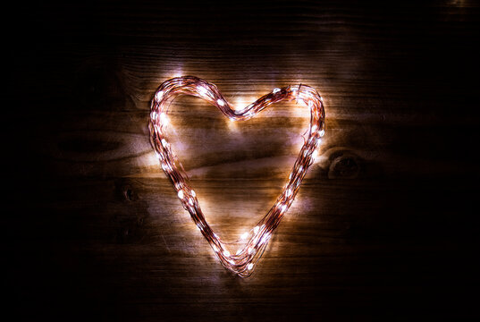 A heart shaped figure laid out light LED garland on vintage brown wooden board. Heart made of LED rice lights. Concept of Valentine Day, strong eternal love, light of love in the heart of a lover