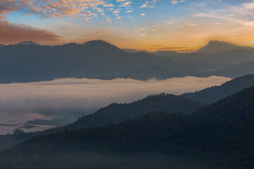 Mountains in clouds at sunrise in summer. Aerial view of mountain peak in fog. Beautiful landscape with high rocks, forest, sky.
