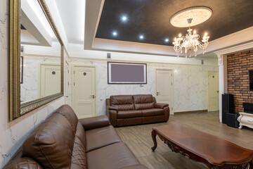 Fototapeta premium interior of a modern living room with two brown leather sofas, a huge mirror in a frame and an expensive beautiful chandelier on the ceiling