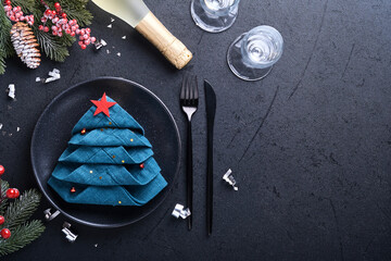 Christmas table setting black color with black silverware, napkin folded as a Christmas tree,...