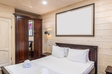 Fototapeta na wymiar interior of a bedroom with a large double bed and a picture above the headboard, finishing the room with natural cream wood, a mahogany wardrobe with a mirror