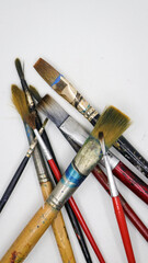 vertical shot of a group of wooden and plastic artists paint brushes different shapes and sizes, with color stains laying on each other isolated in a white background