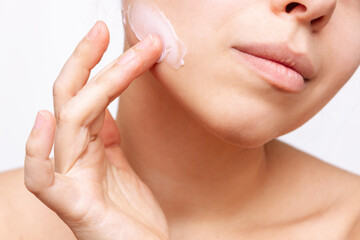 Obraz na płótnie Canvas Cropped shot of a young caucasian woman touching the face with her hand applying a cream on the skin isolated on a white background. Nourishing moisturizing cream. Cosmetology and beauty concept