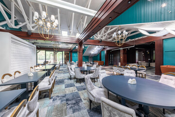 a spacious hall of a luxury restaurant with fashionable modern designer furniture and huge beams made of natural wood under the ceiling, expensive chandeliers and a carpet in a cage