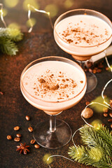 Alexander cocktail in cocktail glass on wooden table with shaker, nutmeg and small grater with Christmas decor on dark background. Beverage photography. Festive cocktail drink.