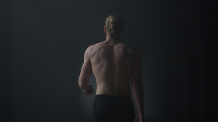 Fototapeta na wymiar Male athlete walking in dark corridor. Sporty guy going in loft building