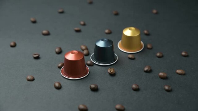 Camera travels over table with coffee beans, coloured coffee capsules, a coffee bag. espresso coffee capsules panning. Tracking shot of several coffee capsules. On black bacground.